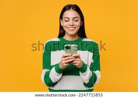 Young smiling brunette latin woman wear casual cozy green knitted sweater hold in hand use mobile cell phone in mint case isolated on plain yellow background studio portrait People lifestyle concept Royalty-Free Stock Photo #2247715855