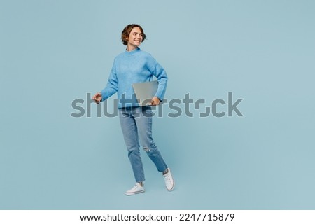 Full body smart young IT woman wearing knitted sweater hold closed laptop pc computer look aside on workspace area isolated on plain pastel light blue cyan background studio. People lifestyle concept