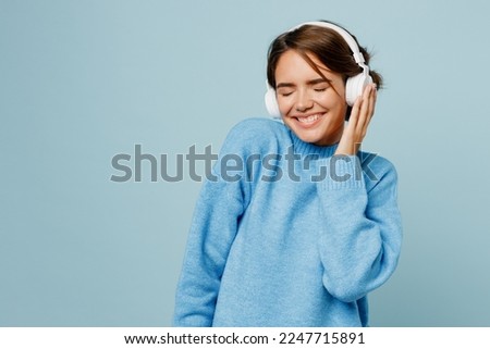 Young satisfied fun woman wear knitted sweater headphones listen to music raise up hands dance close eyes isolated on plain pastel light blue cyan background studio portrait. People lifestyle concept Royalty-Free Stock Photo #2247715891