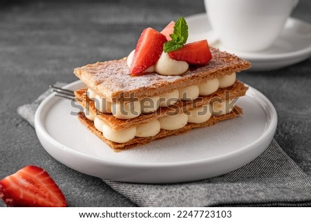 French dessert millefeuille with vanilla cream and fresh strawberries on a white plate on a dark concrete background