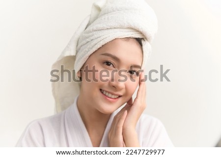 Close up portrait photo of young beautiful Asian woman taking care of her facial skin after apply face skin care cosmetic lotion moisturizer product and checking in mirror at home. Beauty care concept