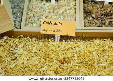 Marigold flowers for sale at the municipal market in a wooden box with the sign and the price in euros per 50 grams. Calendula flower. Calendula medicinal herb - Calendula officinalis.