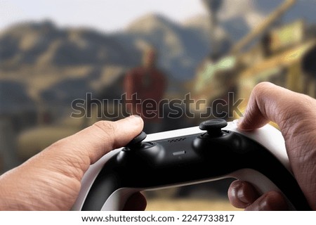 Video games. A gamepad in the hands of a gamer against the background of a video game on a large TV screen. Modern technologies, electronics, video games, online games with friends.