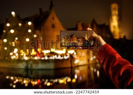 Taking picture of Belgium old town Brugge illuminated at night. Tourist with smartphone