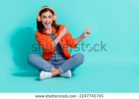 Full length photo of cute impressed girl dressed shirt enjoying music pointing empty space isolated turquoise color background