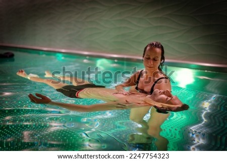 Therapeutic exercise in the pool. Woman receiving an aquatic therapy in the pool. Water relaxation and deep meditation. Royalty-Free Stock Photo #2247754323