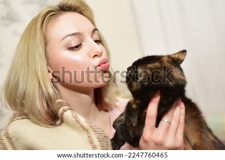 Lady holds a cute cat in her hands and tries to kiss this fluffy cutie.