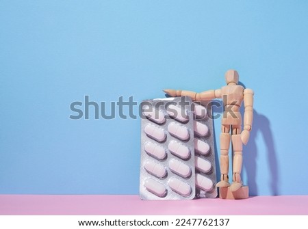 Oval pills in a blister pack and a wooden puppet man on a blue background