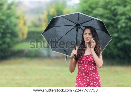 Ethnic woman with umbrella having phone argument in park on rainy day	