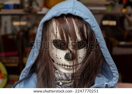 A girl with dark hair in a terrible mask for Halloween on a blurry background in an apartment, close-up, selective focus.