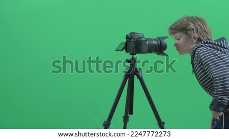 Funny blonde hair child play with big photo camera, green background