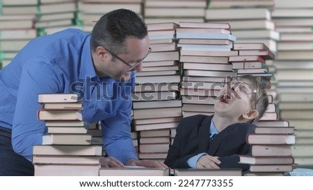 Education can be fun, man teaches young laughing student the amusing part of the homework in front of huge stack of books