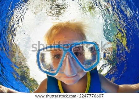 Happy little kid in snorkeling mask jump and dive underwater in coral reef sea lagoon. Family travel lifestyle in summer adventure camp. Swimming activities on beach vacation with child.