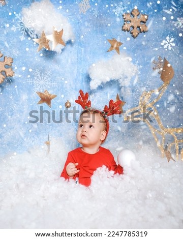 Little girl in dress in the winter forest. Winter wonderland setup with snow, stars and Christmas deer props. 