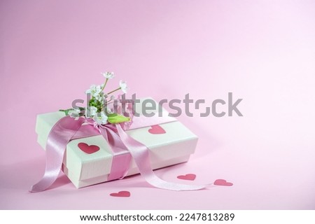 Gift box with flower bouquet, ribbon and paper heart shapes on a light pink background, love greeting card for Valentines day, Mothers day or Wedding, copy space, selected focus, narrow depth of field