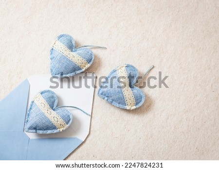 One envelope with three drop-down hearts made of textile with openwork stripes on a background of natural beige stone, flat close-up. Valentine's day concept.