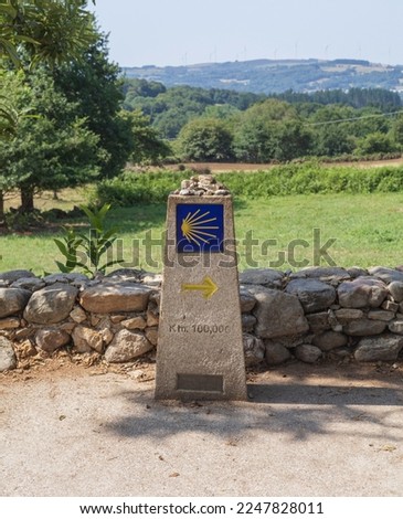 The road sign totem with the yellow shell and arrow, that guides the pilgrims along the Camino de Santiago in Galicia, Spain. It shows how many kilometers are left to reach Santiago de Compostela. Royalty-Free Stock Photo #2247828011