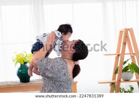 Side view asian mother and newborn baby play together at home, mom holding adorable infant in air and looking with love and tender. Spend time together. women making funny faces to toddler.