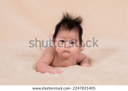 Asian newborn baby 3 month lying prone on beige soft bed. healthy adorable infant without clothes looking for mom want to play with mother while she work, baby feel hungry want milk. healthy toddlers.