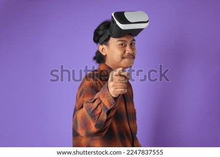 Potrait of young asian man persuade expression using  vr headset pc gadget play pc game with joystick console isolated on purple background studio.
