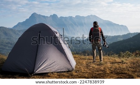 Photographer stands holding a camera looking at the mountain landscape. Travel concept adventure active vacations outdoor