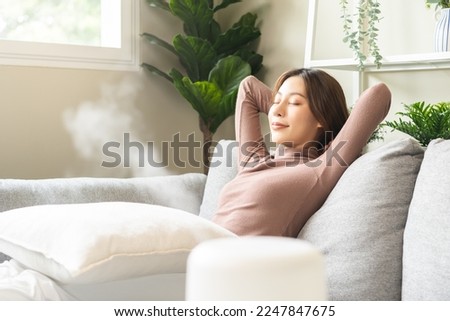Modern air humidifier during relax or rest, happy asian young woman, girl enjoying aromatherapy steam scent from essential oil diffuser comfortable in living conditions room, apartment at home. Royalty-Free Stock Photo #2247847675