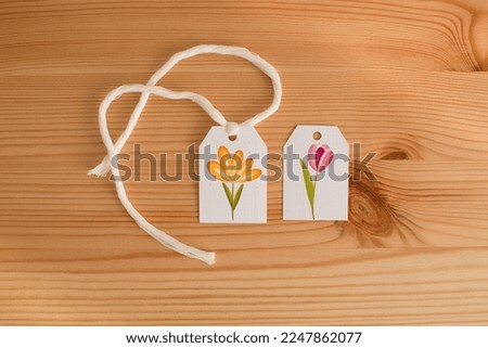 A tag with a picture of a flower on a wooden table, top view.