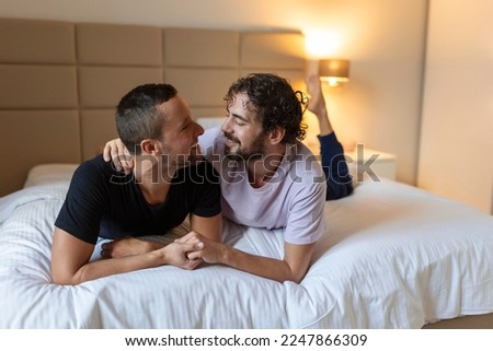 Gay couple embracing each other. Two young male lovers touching their faces together while lying in bed in the morning. Affectionate young gay couple bonding at home.
