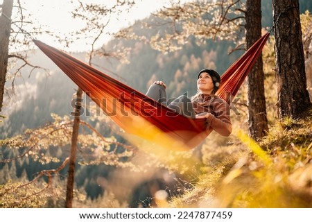Woman with cap resting in comfortable hammock during sunset. Relaxing on orange hammock between two trees pine enjoying the view