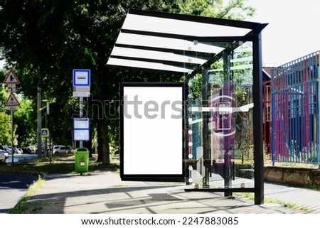 blank white lightbox and glass bus shelter at busstop. empty vertical outdoor billboard. mockup base. lush green street setting. urban background. place holder for poster and advertising or ad display