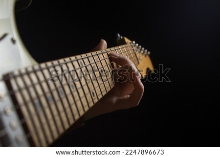 Female hand on the fretboard of an electric guitar on a black background. To play guitar Royalty-Free Stock Photo #2247896673