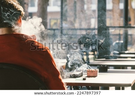Back view of man smoking tobacco cigarette in cafe. Unhealthy lifestyle.  Royalty-Free Stock Photo #2247897397
