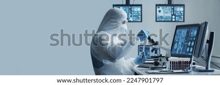 Scientist in protection suit and masks working in research lab using laboratory equipment: microscopes, test tubes. Coronavirus 2019-ncov hazard, pharmaceutical discovery, bacteriology and virology. Royalty-Free Stock Photo #2247901797