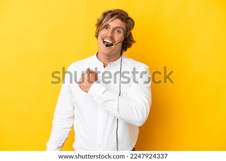 Telemarketer man working with a headset isolated on yellow background celebrating a victory