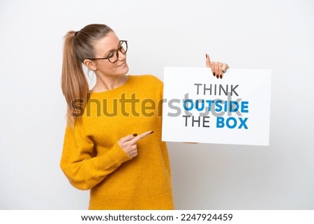 Young caucasian woman isolated on white background holding a placard with text Think Outside The Box and  pointing it