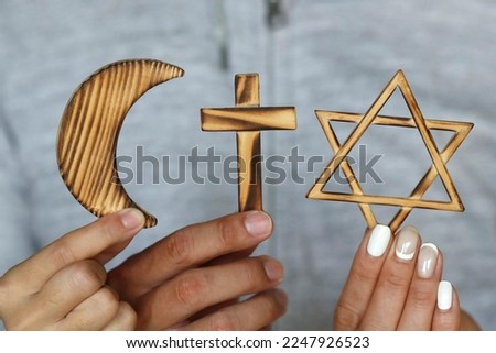 Religious symbols in three hands. Jewish Star of David, Muslim star and Crescent, Christian Cross. Religion, interreligious  and interfaith dialogue concept.  Royalty-Free Stock Photo #2247926523
