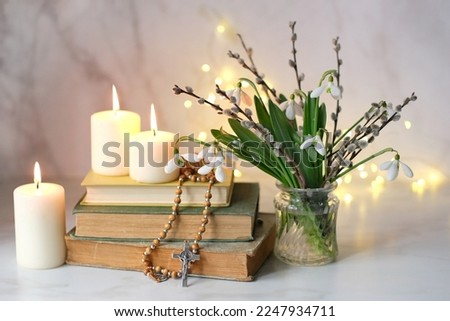 Bouquet of Snowdrop flowers with willow branches, christian rosary beads, books and candles on table, abstract background. Religious church holiday. symbol of faith in God, Easter, Palm Sunday
