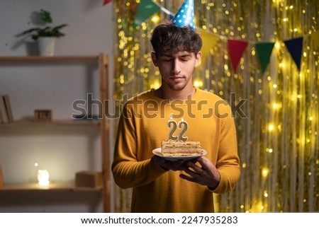 Guy celebrating 22st birthday at home, holding a cake with candles and making a wish, copy space