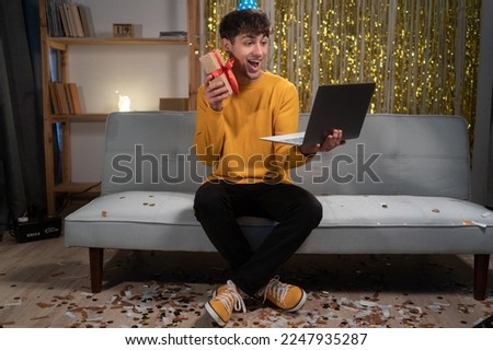 Guy holding birthday gift having video call via laptop, celebrating his birthday online with remote friends at home. Distance holiday celebration, virtual party concept. Copy space