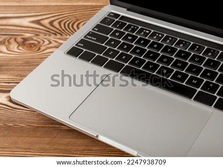 Laptop keyboard with black buttons on a silver background. Laptop on a brown wooden table. Keyboard of a modern laptop.