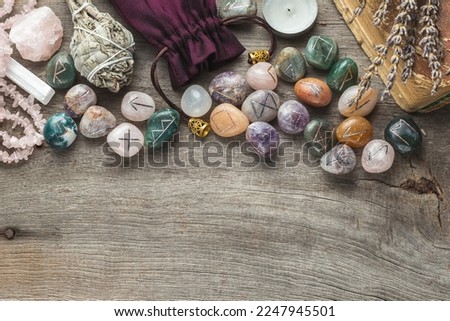 Elder Futhark Rune Stones Set Made of Natural Gemstones, Sage Incense, Candle, Old Book on Wooden Background Royalty-Free Stock Photo #2247945501