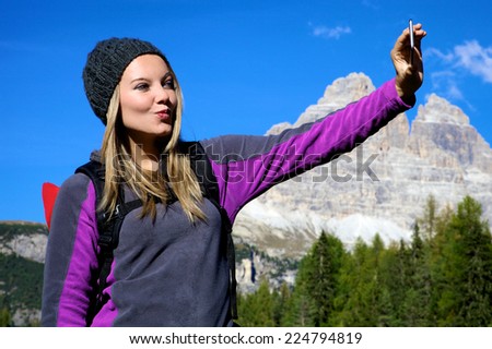 happy beautiful blond girl tacking selfie photo during vacation in mountain sanding a kiss