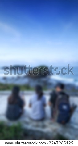 Blurred photo of three people sitting on a wavy beach with a blue sky.