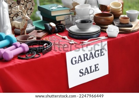 Paper with sign Garage sale and many different items on red tablecloth outdoors