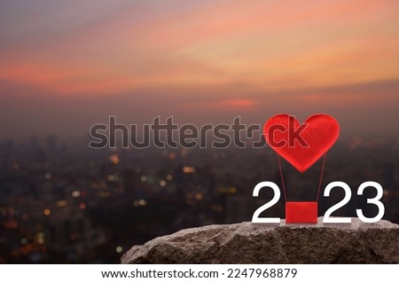 Red fabric heart love air balloon with 2023 white text on rock mountain over cityscape on warm light sundown, Happy new year and Valentines day 2023 concept