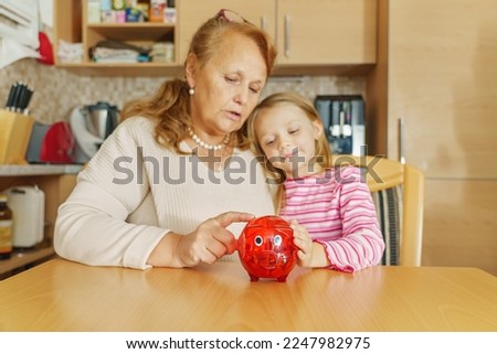 Grandma and a little girl with a piggy bank in the middle. Count and put money back. in generating. Learn to save together.