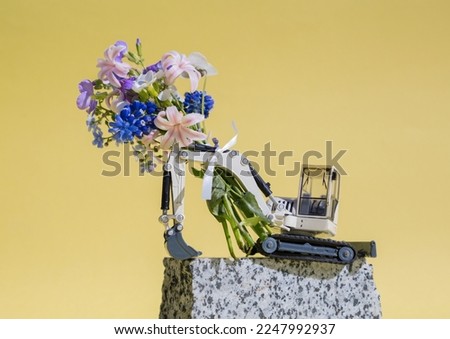 congratulation, postcard for construction business. bouquet of flowers on excavator boom. toy machine - excavator near piece of granite on yellow background. builder's day holiday