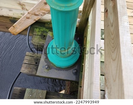 The bottom of a green pole that has been bolted into the side of a bridge.