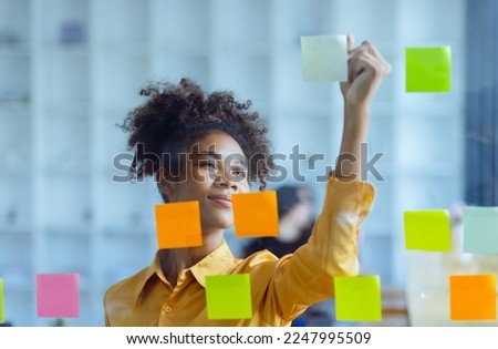 Young African American stylish woman working on project plan using sticky papers notes on glass wall, people meeting to share idea, Business design planning concepts. Royalty-Free Stock Photo #2247995509