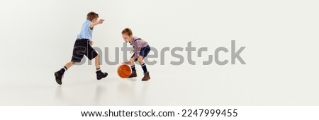 Two boys, children in classical retro clothes playing basketball over grey studio background. Banner, flyer. Concept of game, childhood, friendship, activity, leisure time, retro style, fashion.